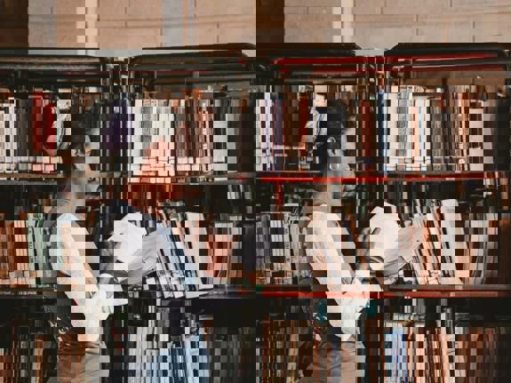 Woman Looking Through a Book at the Library Bookcases